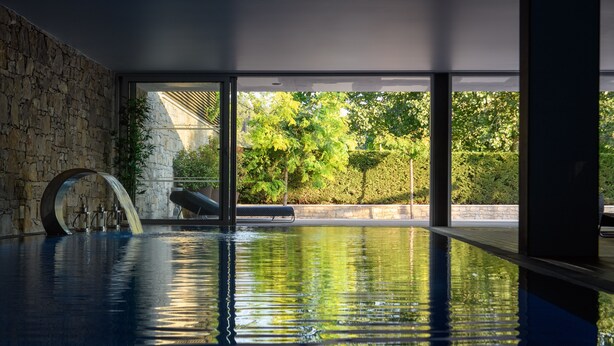 An indoor swimming pool with a stone wall, a bench, and a view of greenery outside. - Hotel de Charme Casa da Amieira (Santarém)