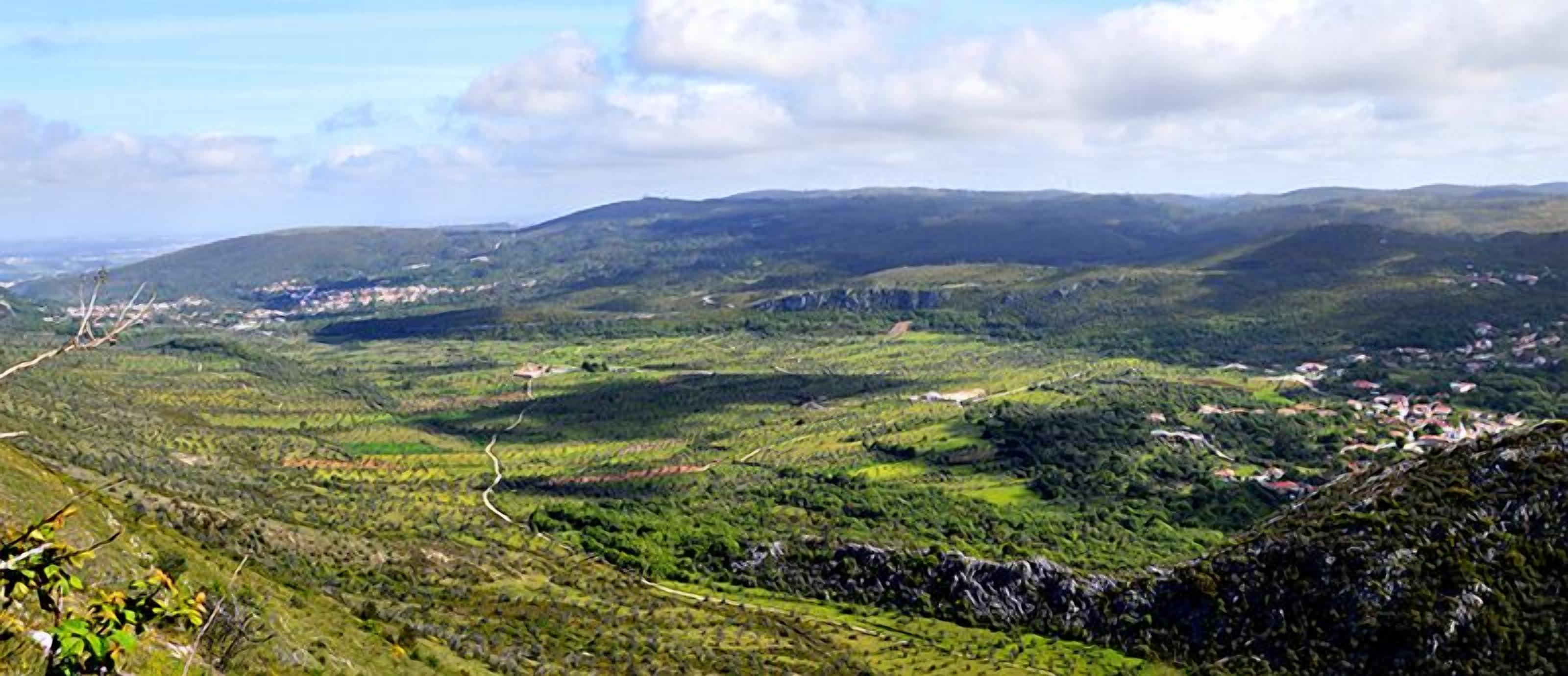 A panoramic view of a mountainous landscape with a winding road and scattered buildings.