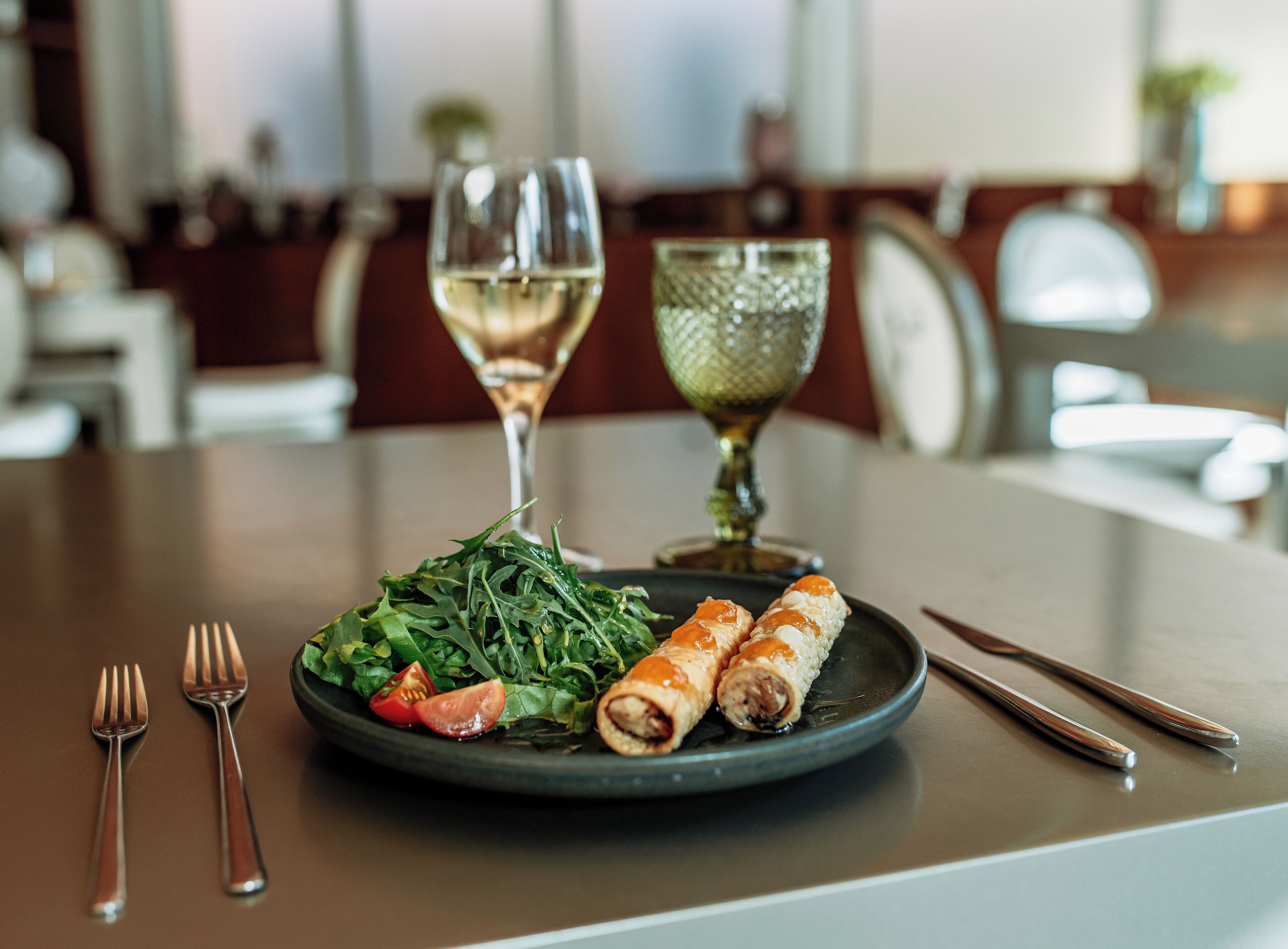 A plate of food with a salad, two rolls, and a glass of white wine on a table.