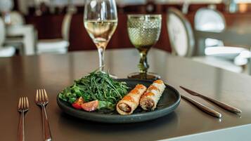 A plate of food with a salad, two rolls, and a glass of white wine on a table.