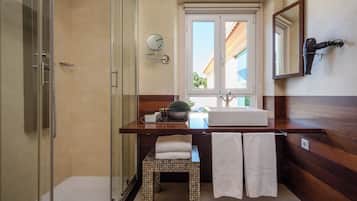 Casa de banho com cabine de chuveiro em vidro, toucador de madeira com lavatório, espelho e porta-toalhas.
