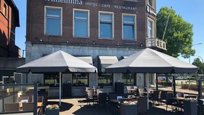 An outdoor seating area with umbrellas and tables in front of the Wilhelmina Hotel Café Restaurant. - Hotel Wilhelmina (Venlo)