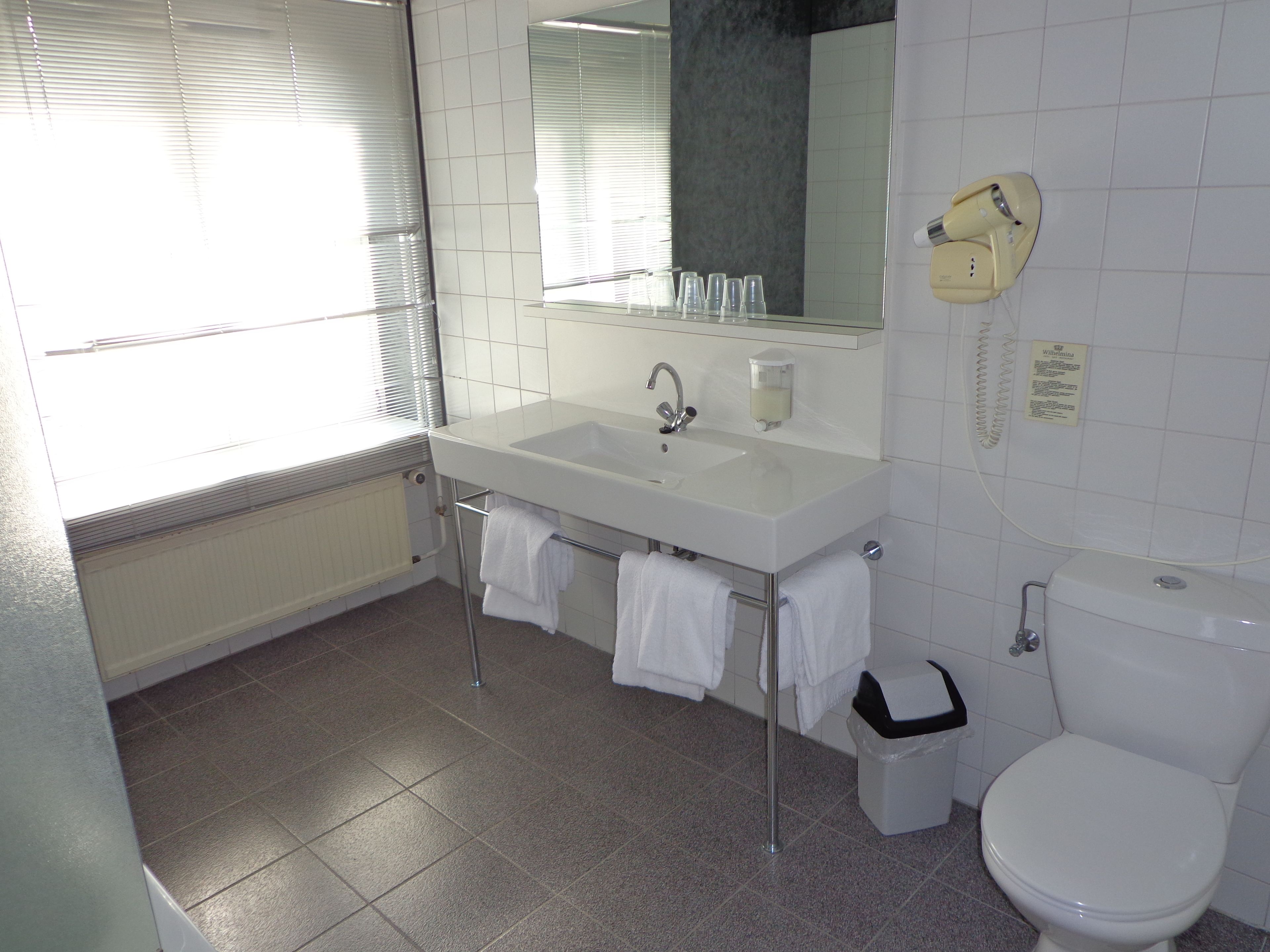 A bathroom with a white sink, mirror, and toilet. There are towels hanging on a rack, and a hairdryer on the wall.