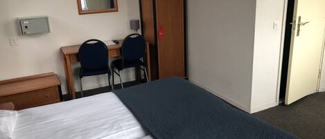 A hotel room with a bed, a desk, two chairs, a wardrobe, a mirror, and a door.