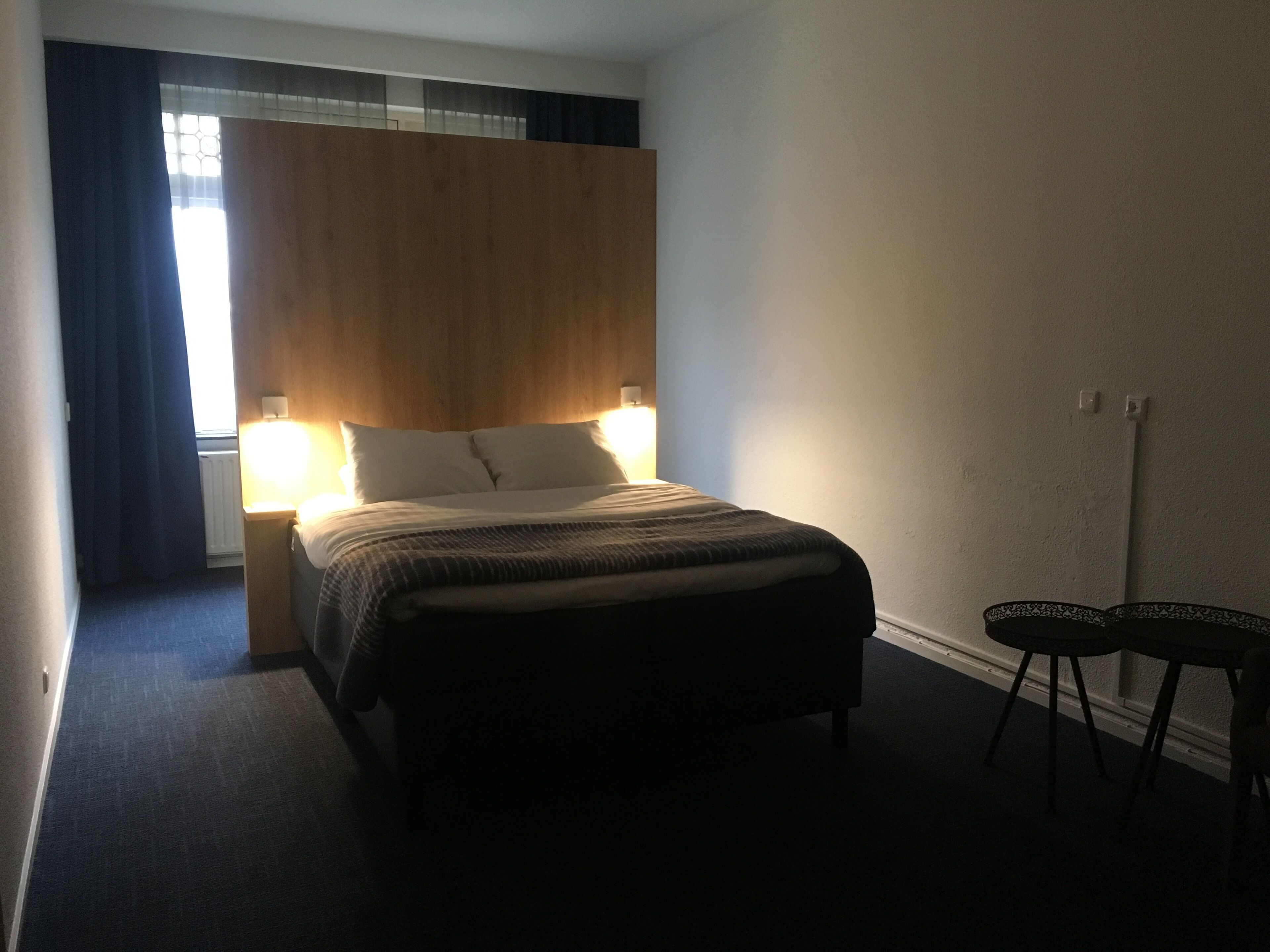 A hotel room with a bed, bedside lamps, a small table, and a chair.
