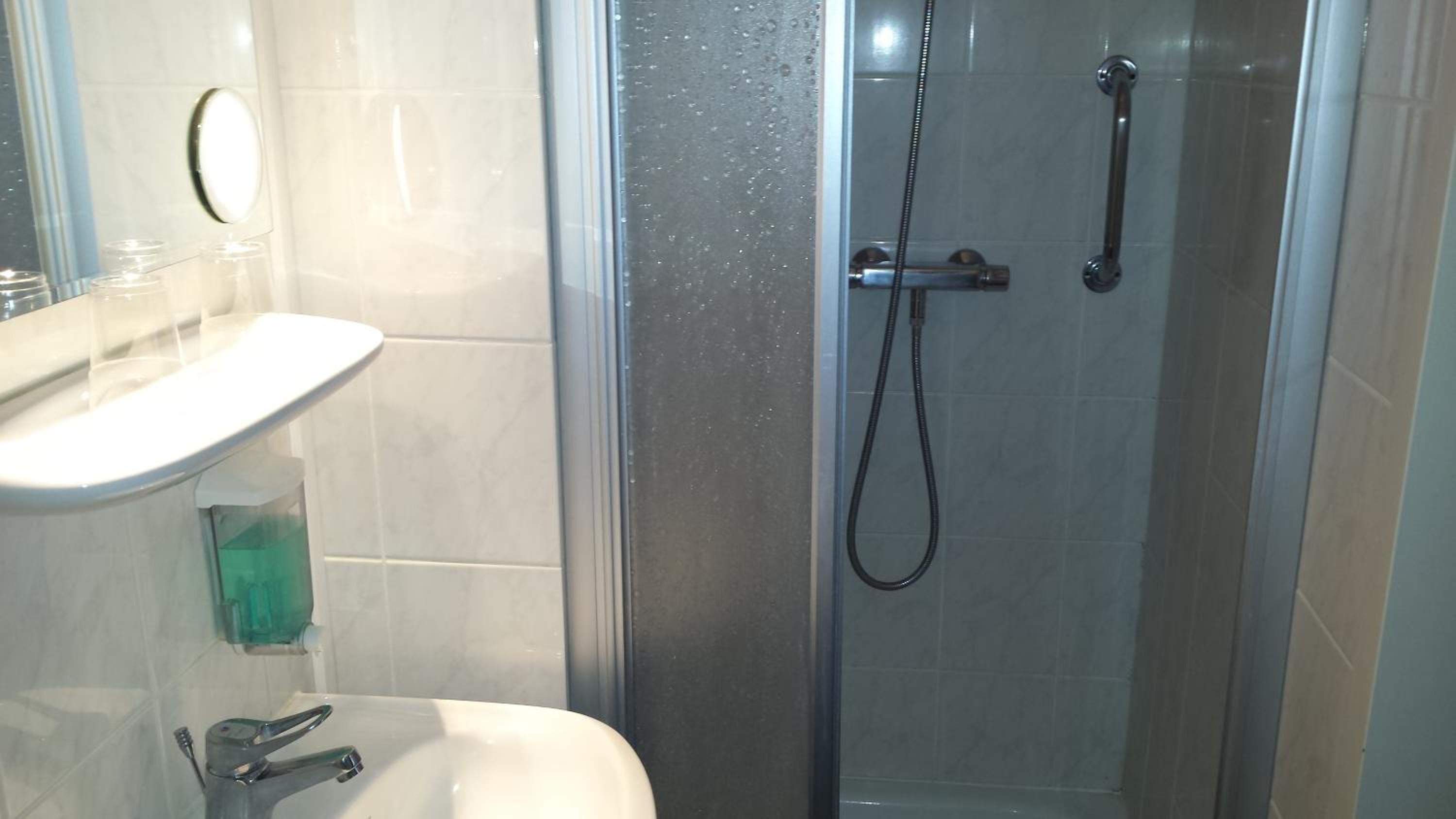 Un baño con ducha de vidrio, un lavamanos blanco y un espejo.