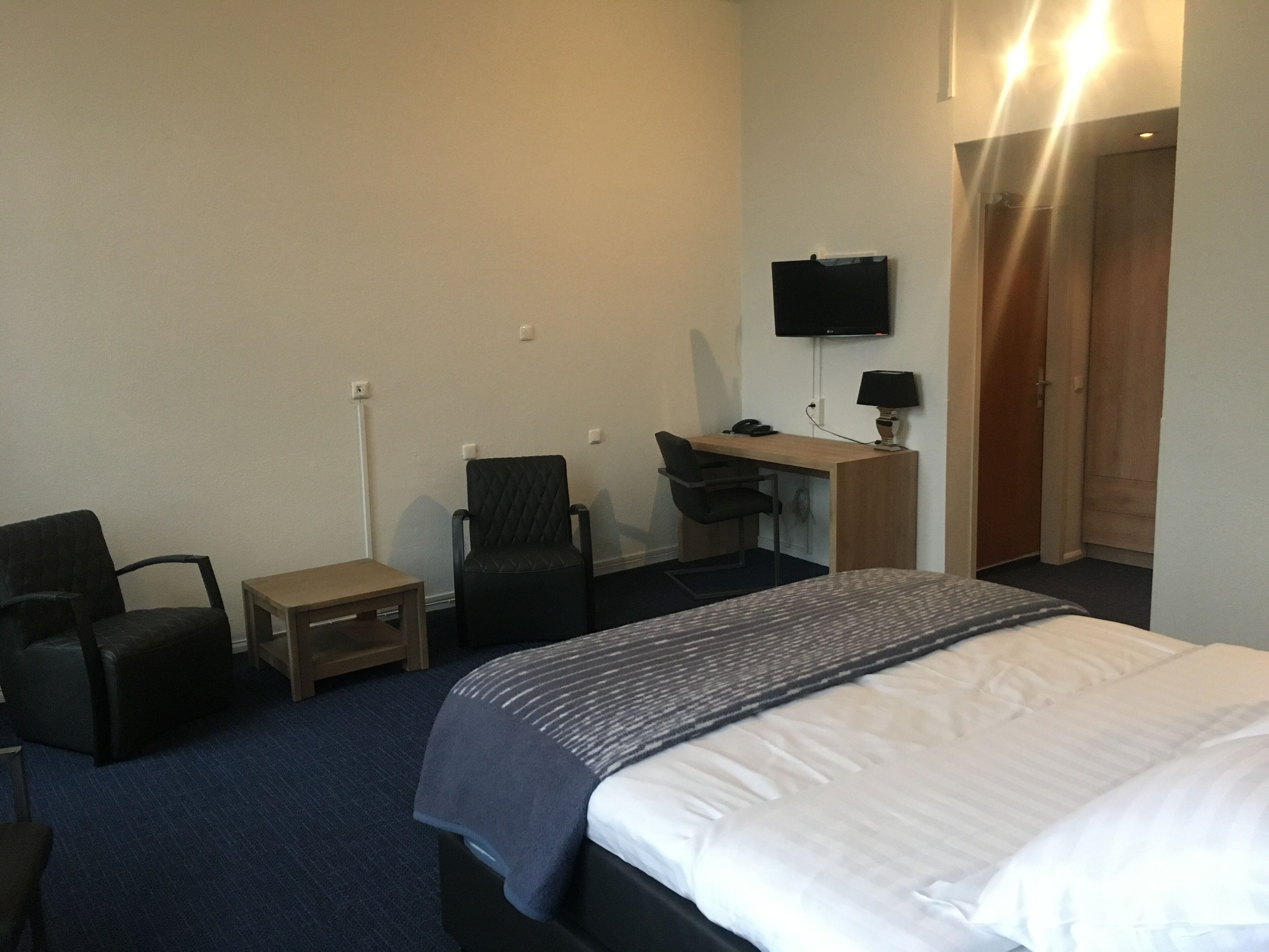 Una camera d'albergo con un letto, una scrivania con un computer, una sedia, un tavolino e una TV fissata al muro.