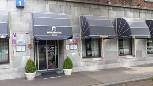 A hotel with a modern facade, featuring large awnings labeled 'Wilhelmina Hotel' and 'Wilhelmina Restaurant'. There are two potted plants at the entrance, and the building has a stone exterior with visible signage for amenities and services. - Hotel Wilhelmina (Venlo)