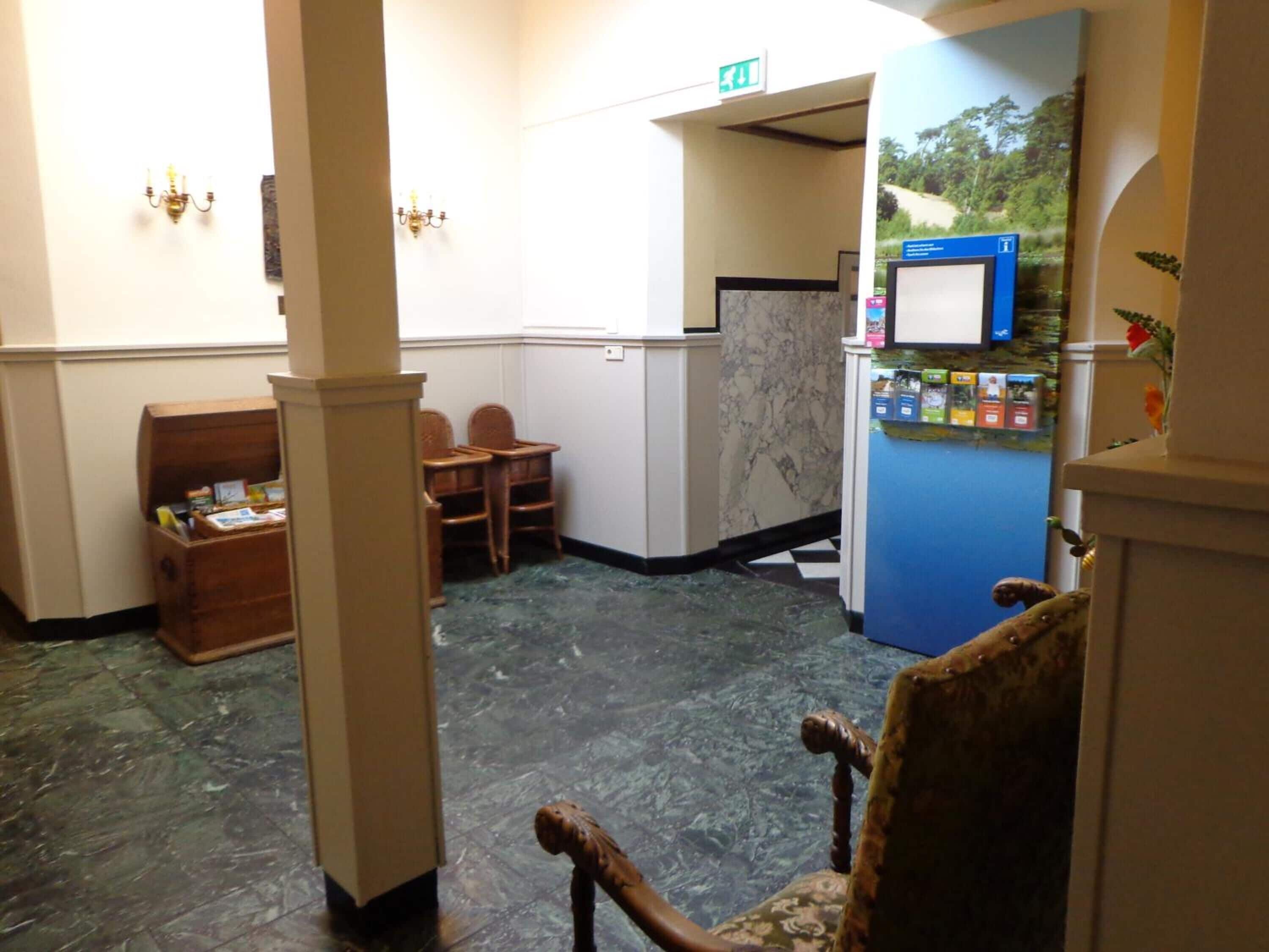 Eine Lobby mit einer Rezeption, einer blauen Verkaufsmaschine, einer Holzkiste und einem gemusterten Sessel.
