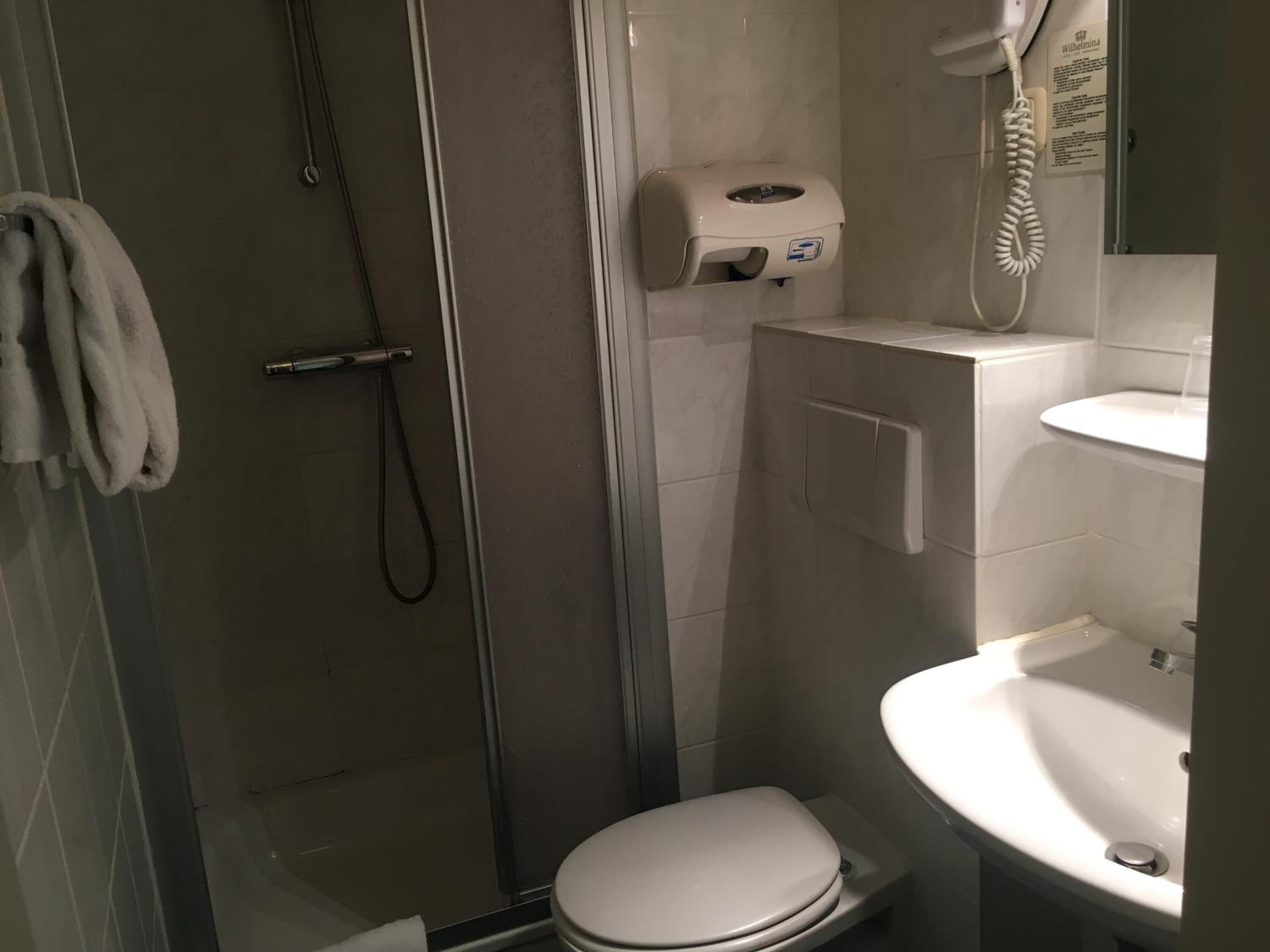 A small, enclosed shower stall with a glass door, a toilet, and a sink with a mirror.