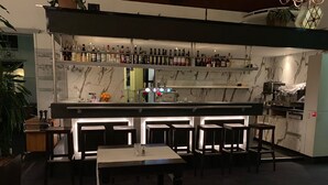 A bar area with a marble countertop, multiple stools, and a variety of bottles and glasses. - Hotel Wilhelmina (Venlo)