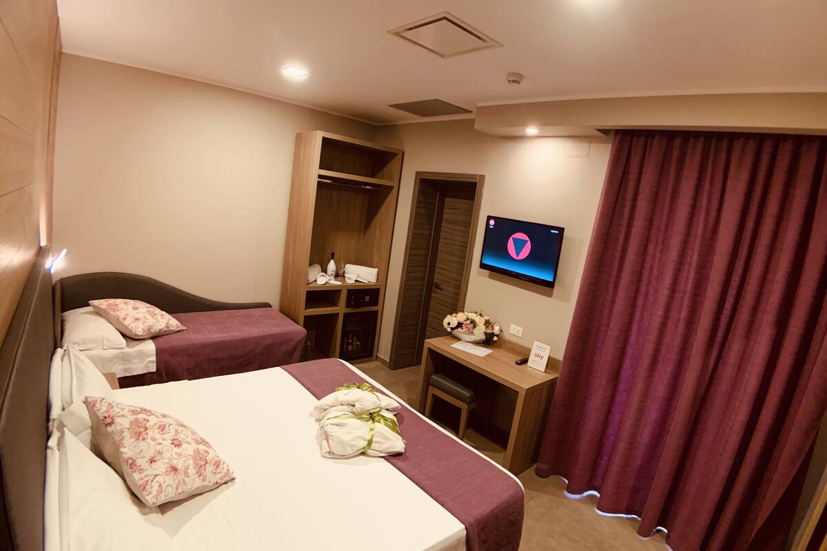 Hotellihuone, jossa on kaksi sänkyä, työpöytä, televisio ja vaatekaappi.