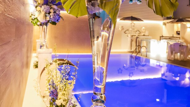 A clear glass vase with a floral arrangement on a table near a pool area. - Hotel Smeraldo (Qualiano)