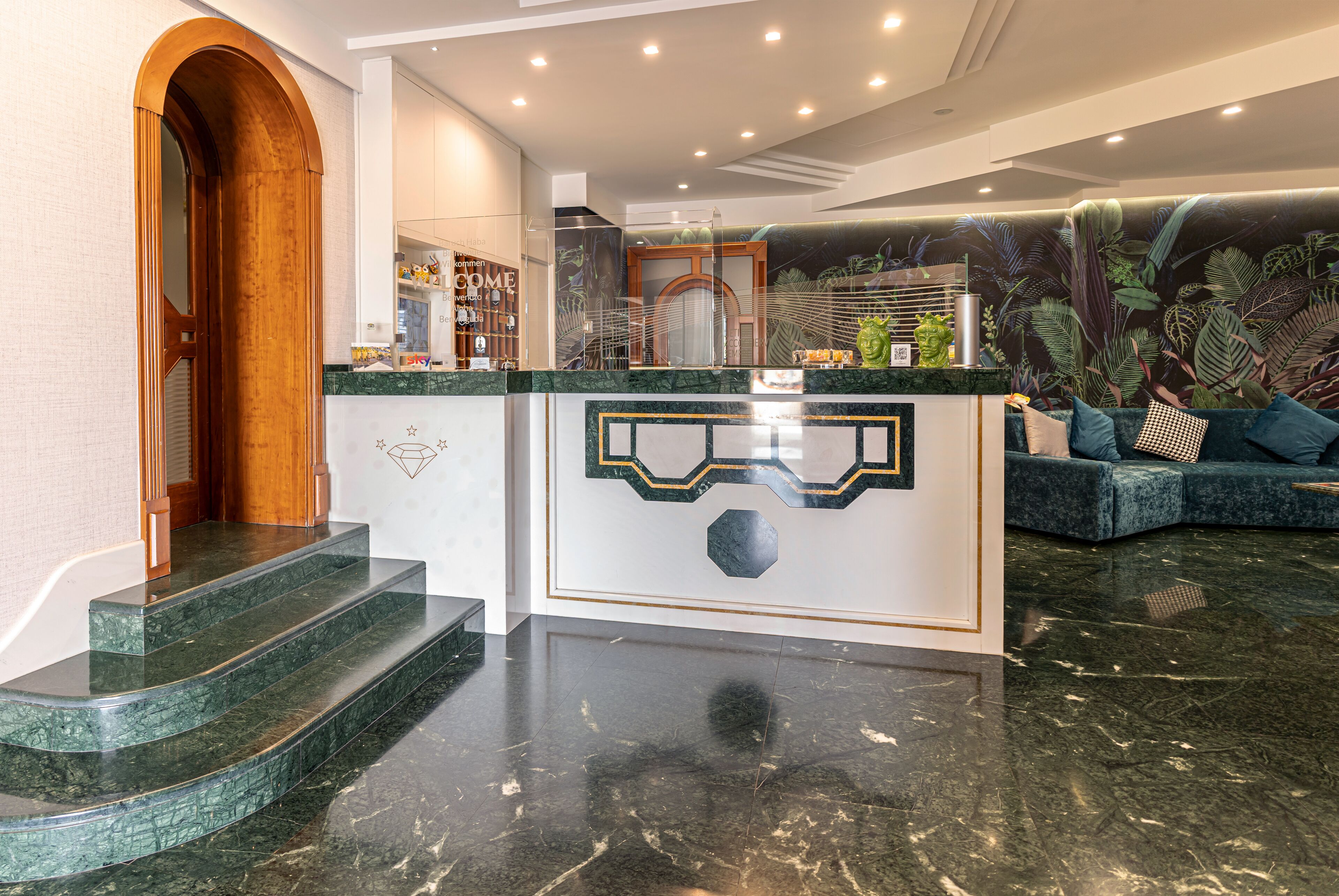 A lobby with a reception desk, a staircase, a seating area, and a wall with a tropical mural.