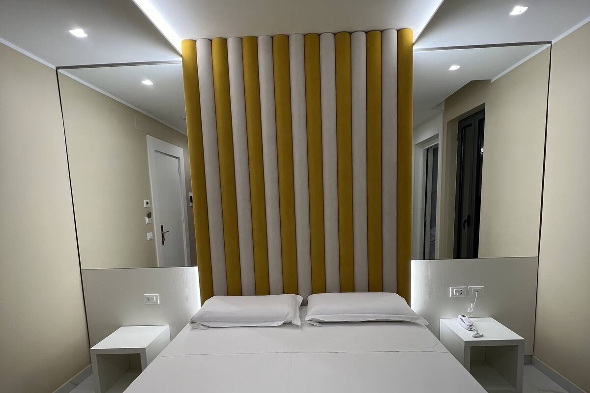 Moderni hotellihuone, jossa on suuri sänky, yöpöytä, yövalaisin ja peili.