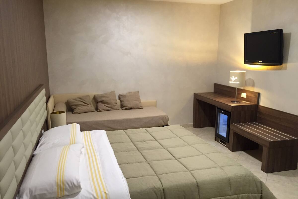 Hotellihuone, jossa on sänky, yöpöytä, lamppu ja seinälle asennettu televisio.