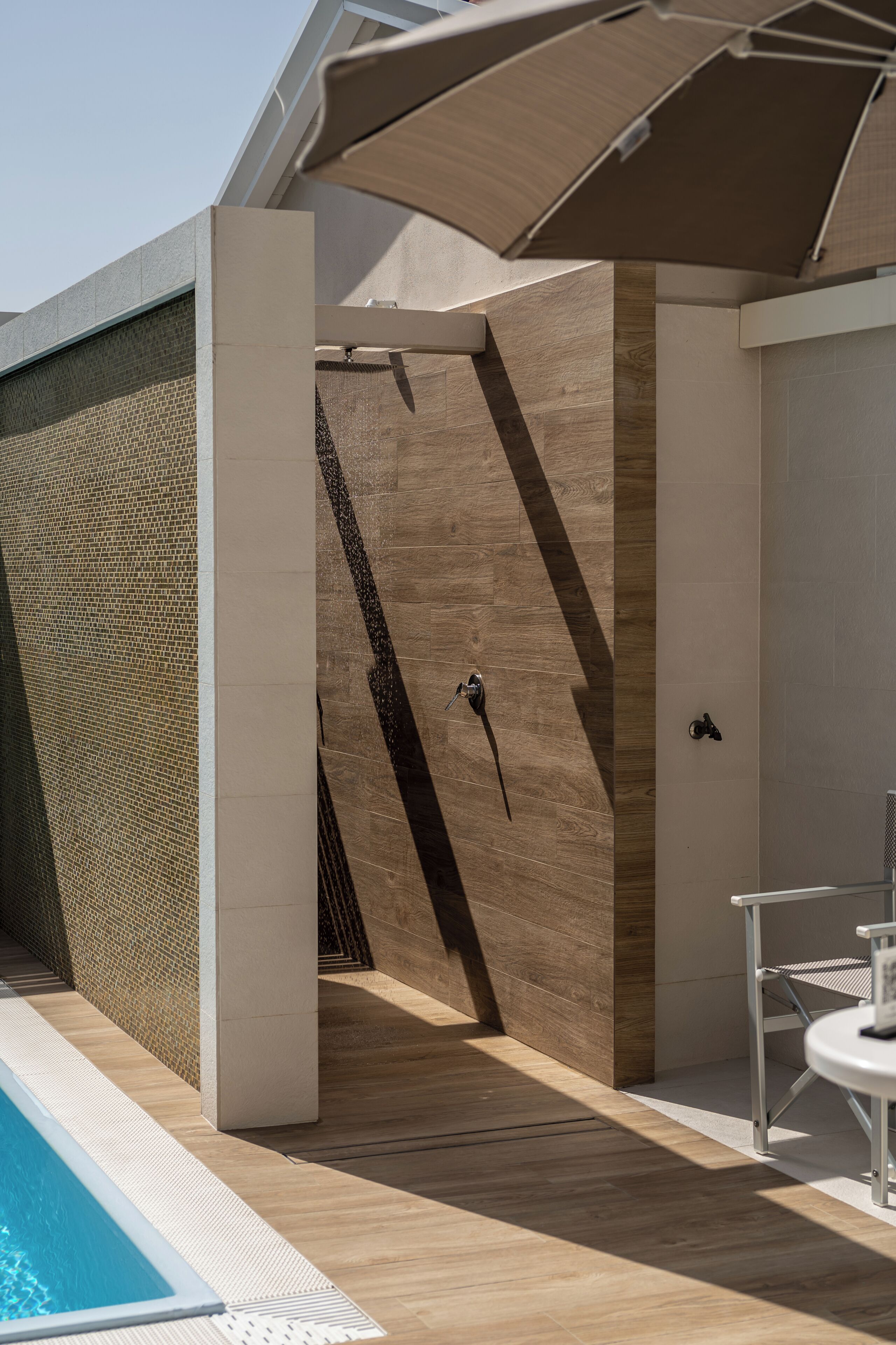 Un espace piscine extérieur moderne, doté d’une terrasse en bois, d’un coin salon couvert et d’un espace de détente au bord de la piscine.