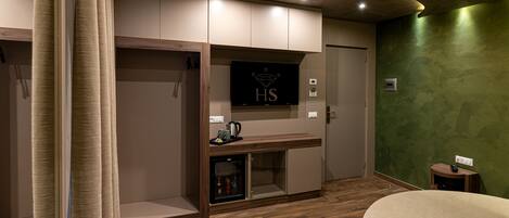 Ein Hotelzimmer mit Holzboden, einem Bett, einem Fernseher, einer Minibar und einer grünen Akzentwand.