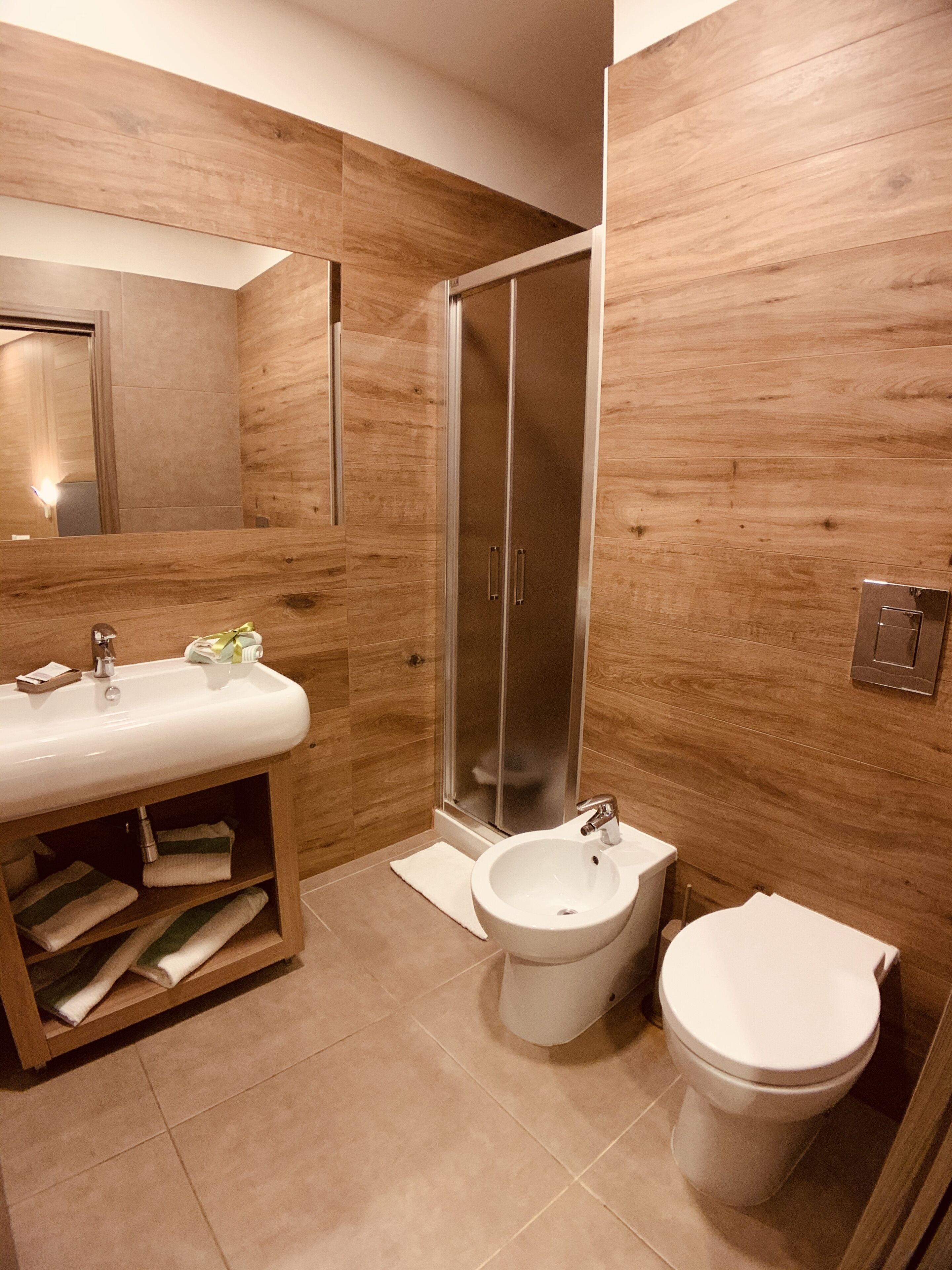 Een moderne badkamer met een houten wastafelmeubel, een douchecabine van glas, een bidet en een toilet.