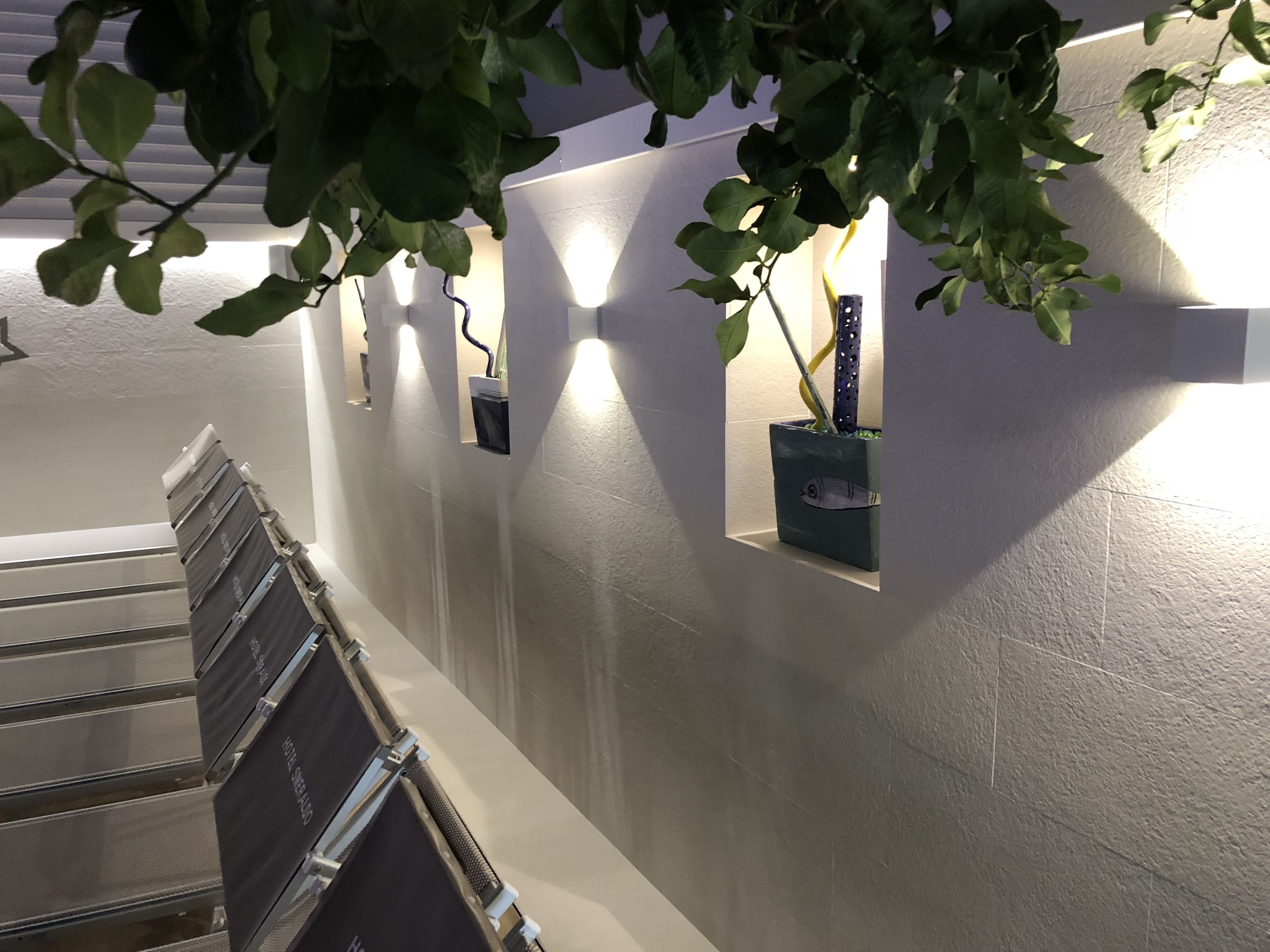 A staircase with a handrail, a wall with recessed planters, and a ceiling with a light fixture.