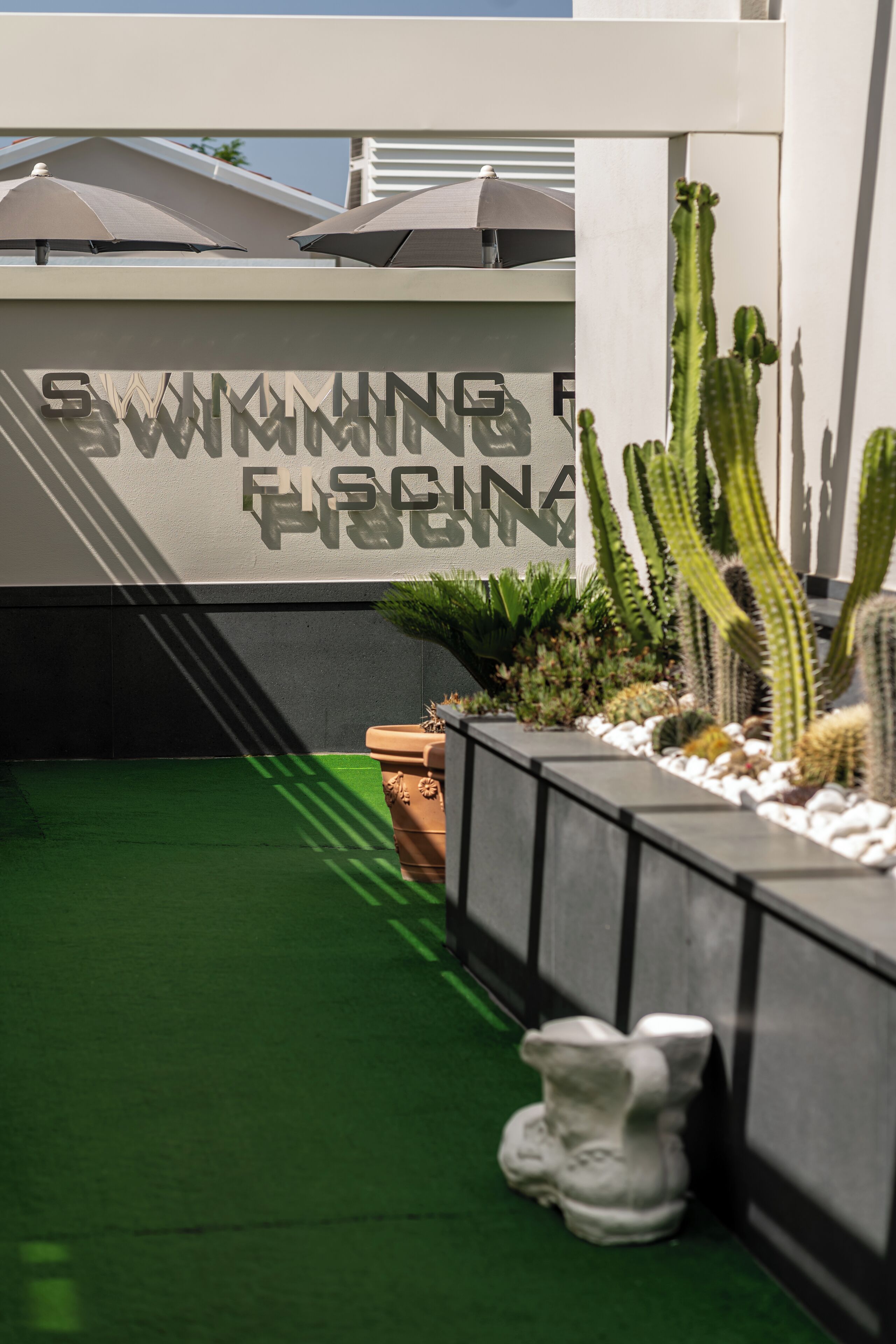 A pool area with a sign reading "SWIMMING FACING PLATINUM," surrounded by cacti and a white sculpture.