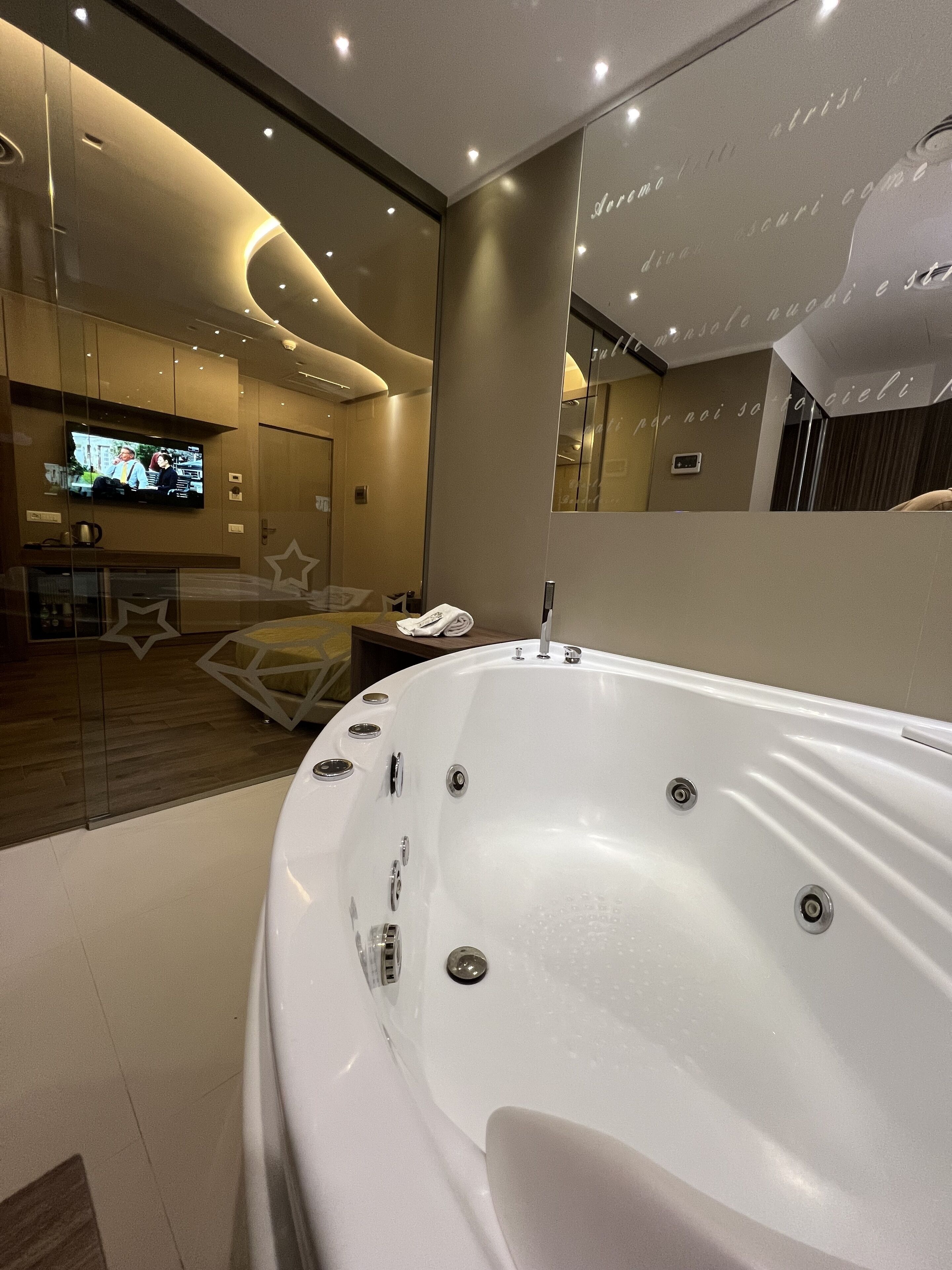Un bagno moderno con una vasca da bagno bianca grande, una televisione montata a parete e uno specchio che riflette l'ambiente.