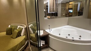 A modern bathroom with a large bathtub, a glass shower enclosure, and a seating area with a sofa and pillows. - Hotel Smeraldo (Qualiano)