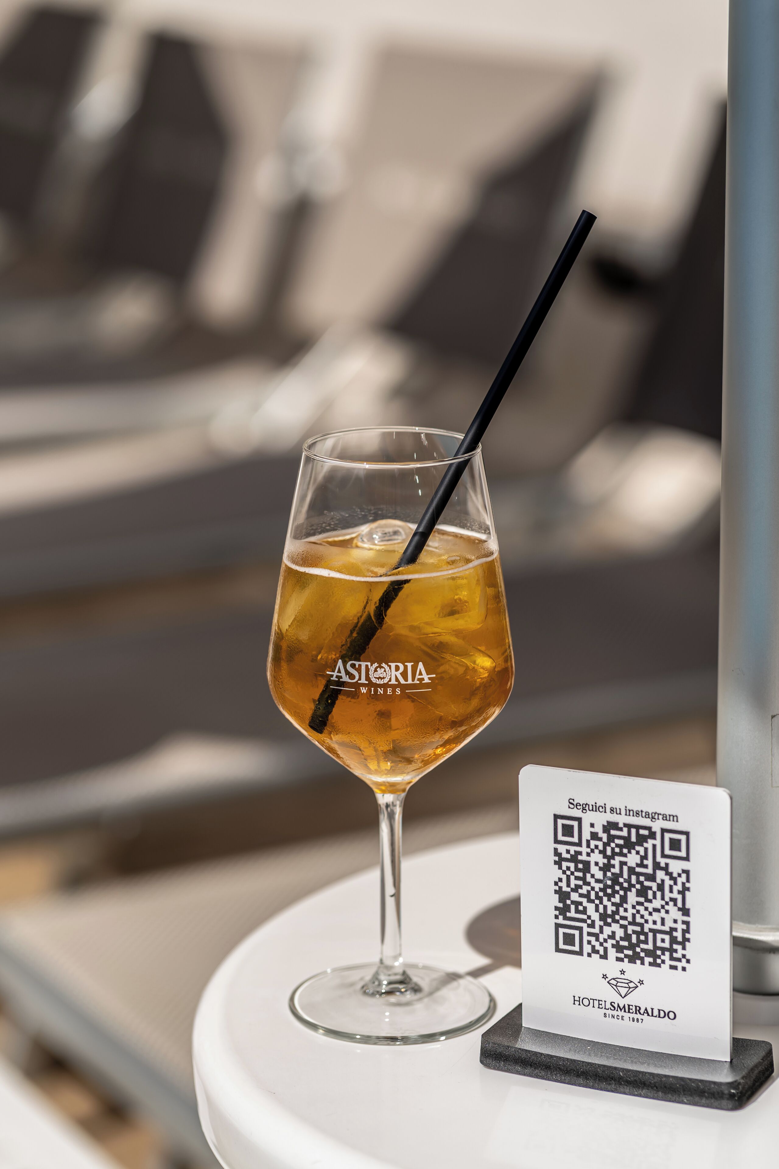 A glass of wine with a straw on a table with a QR code and a sign for ASTORIA WINES.