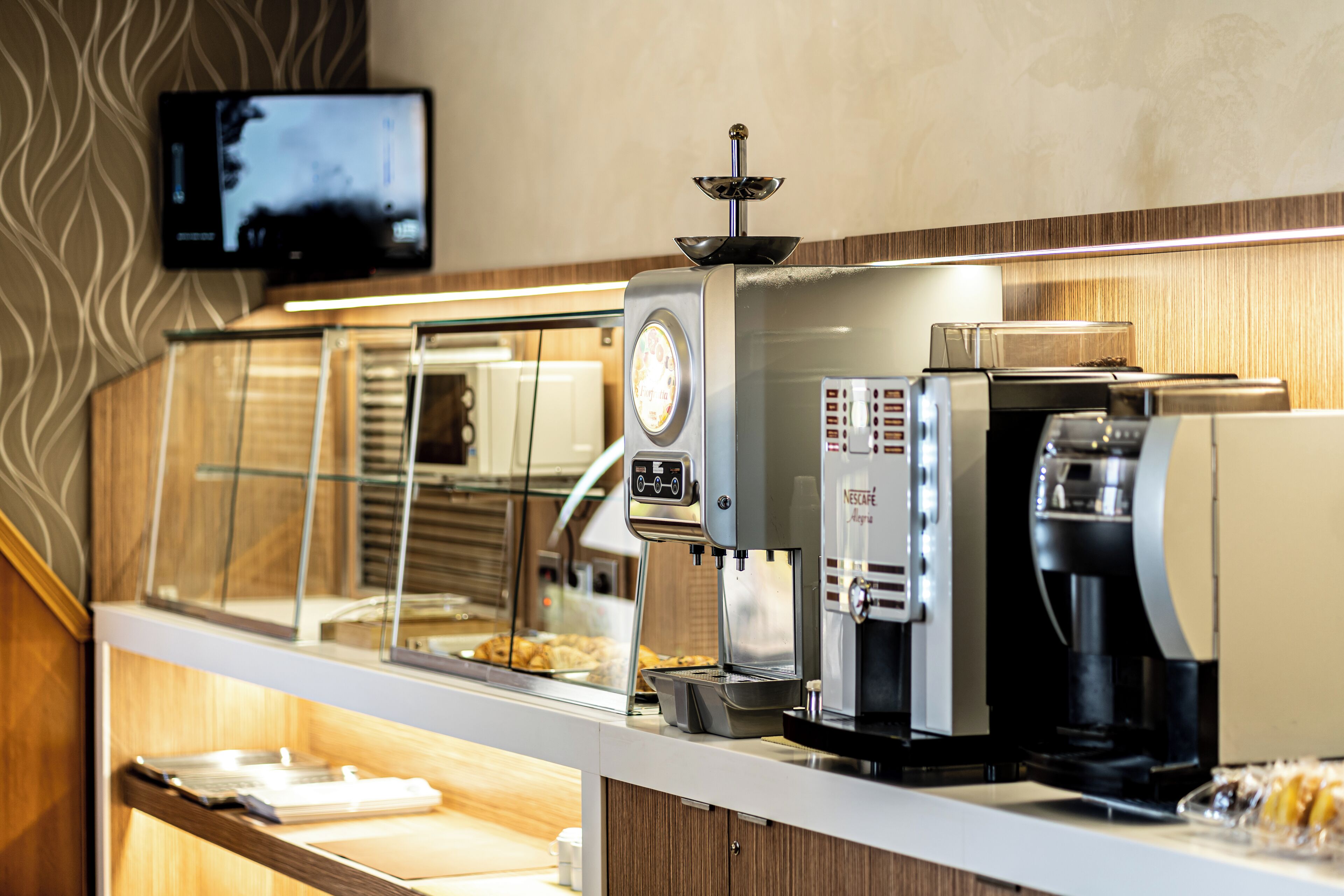A coffee bar with a digital screen, espresso machines, and a display case with pastries.