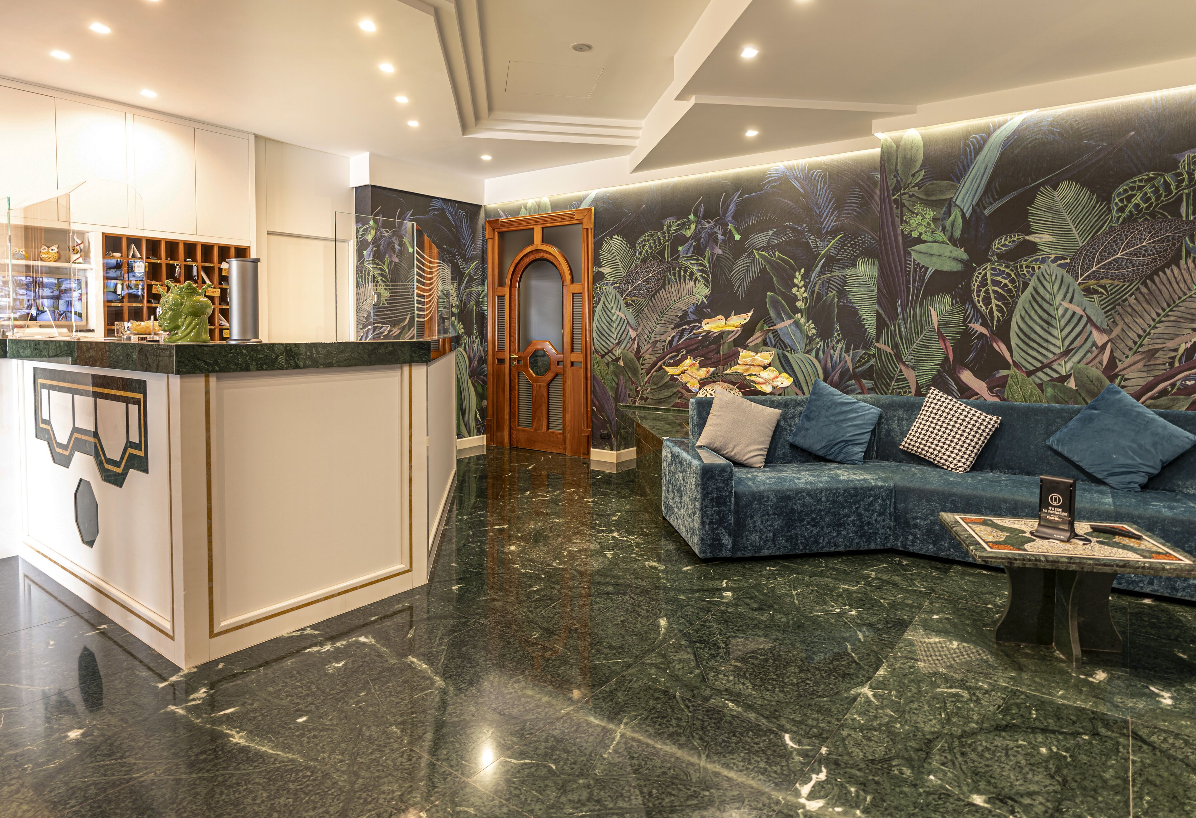 A lobby with a reception desk, a blue sofa, and a mural of tropical foliage.