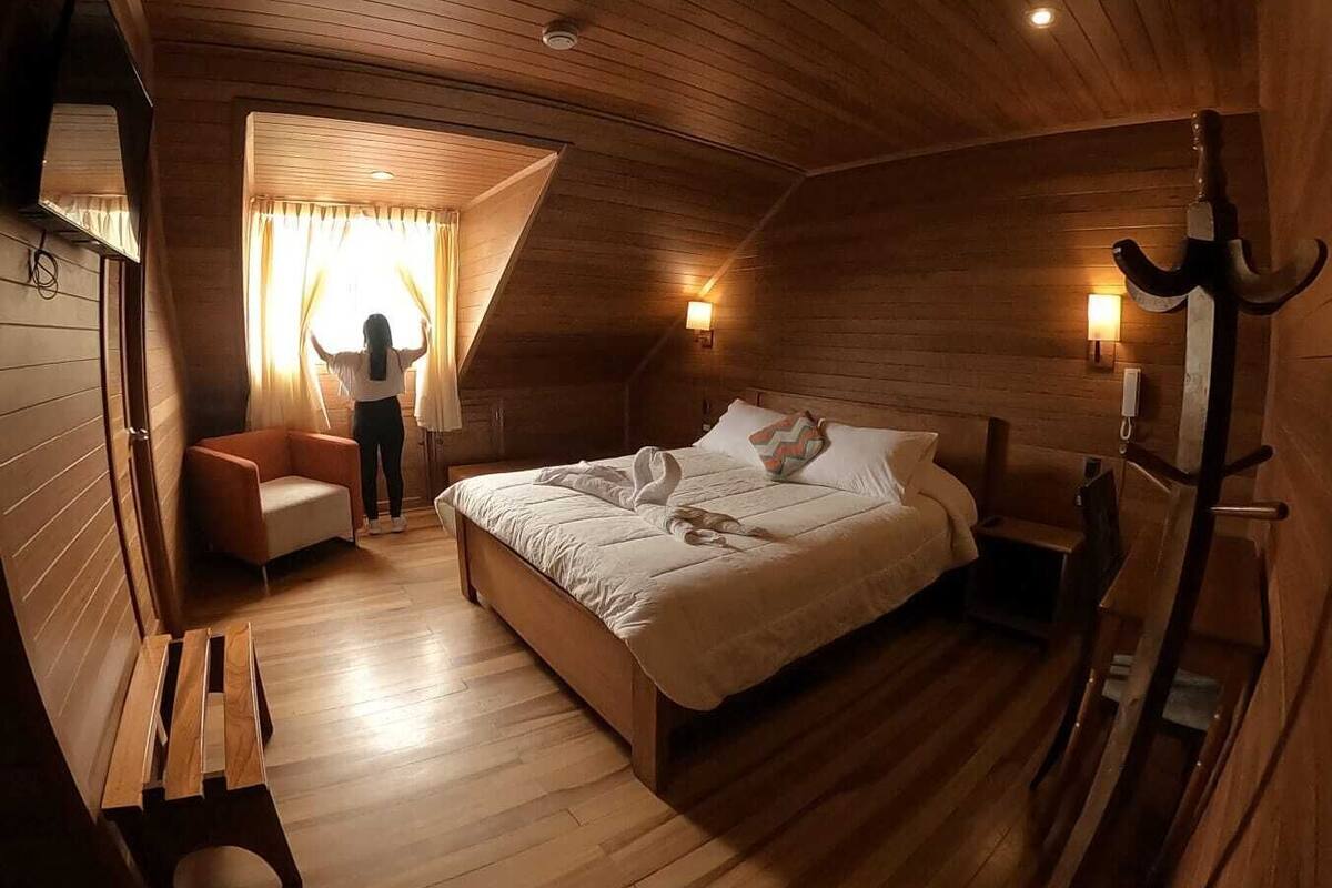 Ein gemütliches Schlafzimmer mit Holzwänden, einem Bett, einem Sessel und einem Schreibtisch.