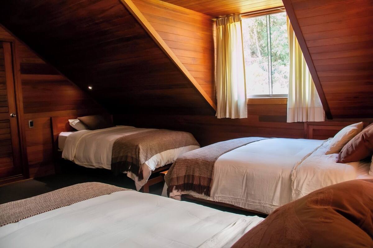 Ein gemütliches Schlafzimmer im Dachgeschoss mit zwei Betten, Holzwänden und einem Fenster mit Vorhängen.