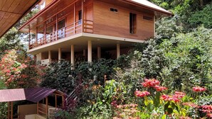 A wooden house with a balcony, surrounded by lush greenery and red flowers. - Hotel Heidinger (Oxapampa)