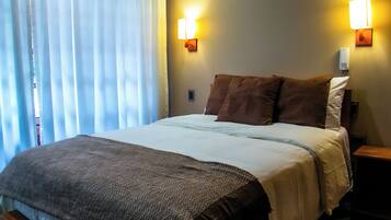 Una cama bien hecha con un edredón estampado, dos lámparas de pared y una mesita de noche.