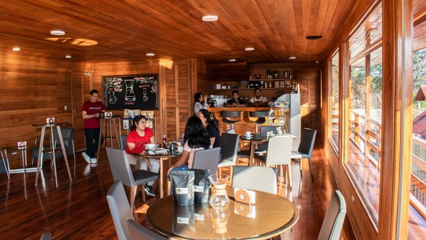 A wooden interior with tables and chairs, a bar area, and large windows. - Hotel Heidinger (Oxapampa)