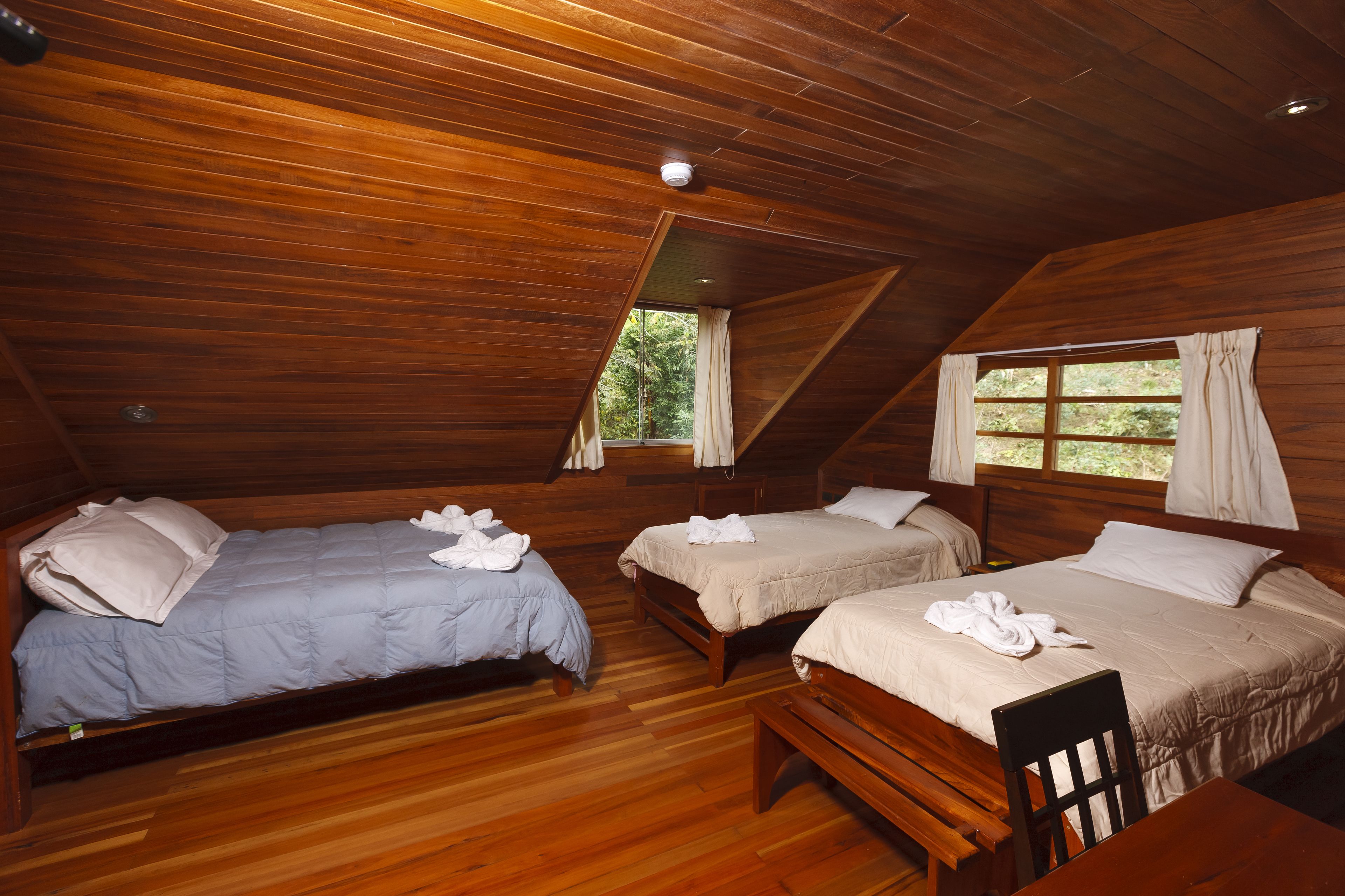 Una cabaña de madera con tres camas individuales, un banco de madera y una mesita.