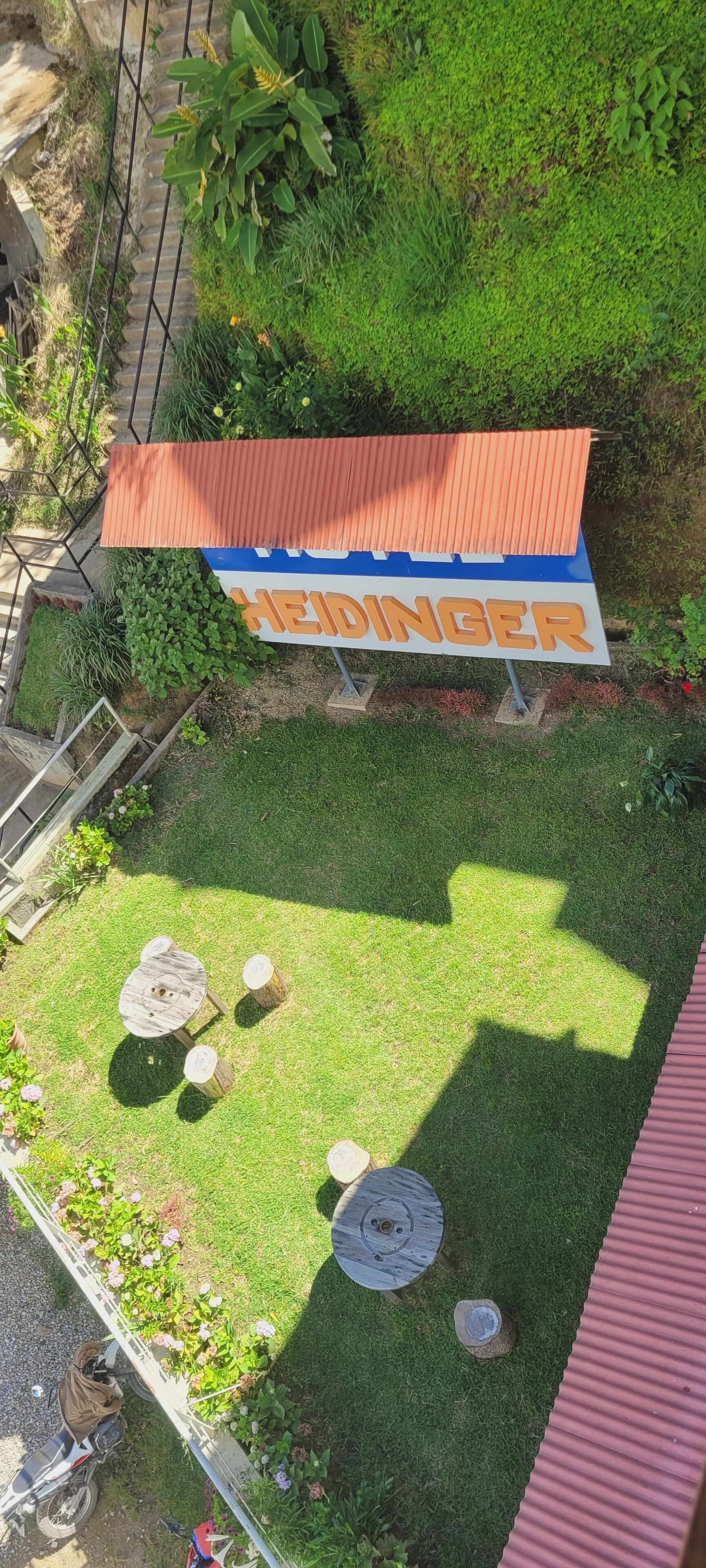 A sign for a restaurant named "HEIDINGER" with a red roof, surrounded by a well-maintained lawn and a small seating area with a table and chairs.