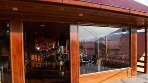 A wooden building with large glass windows and a bar area visible inside. - Hotel Heidinger (Oxapampa)