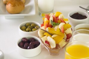 Egy vegyes gyümölcssaláta, mellé egy kanál, valamint tálakban kínált olívabogyó és szőlő, és egy pohár narancslé.
