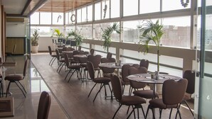 A spacious indoor area with multiple tables and chairs, large windows, and potted plants. - Sunec Hotel (Chiclayo)