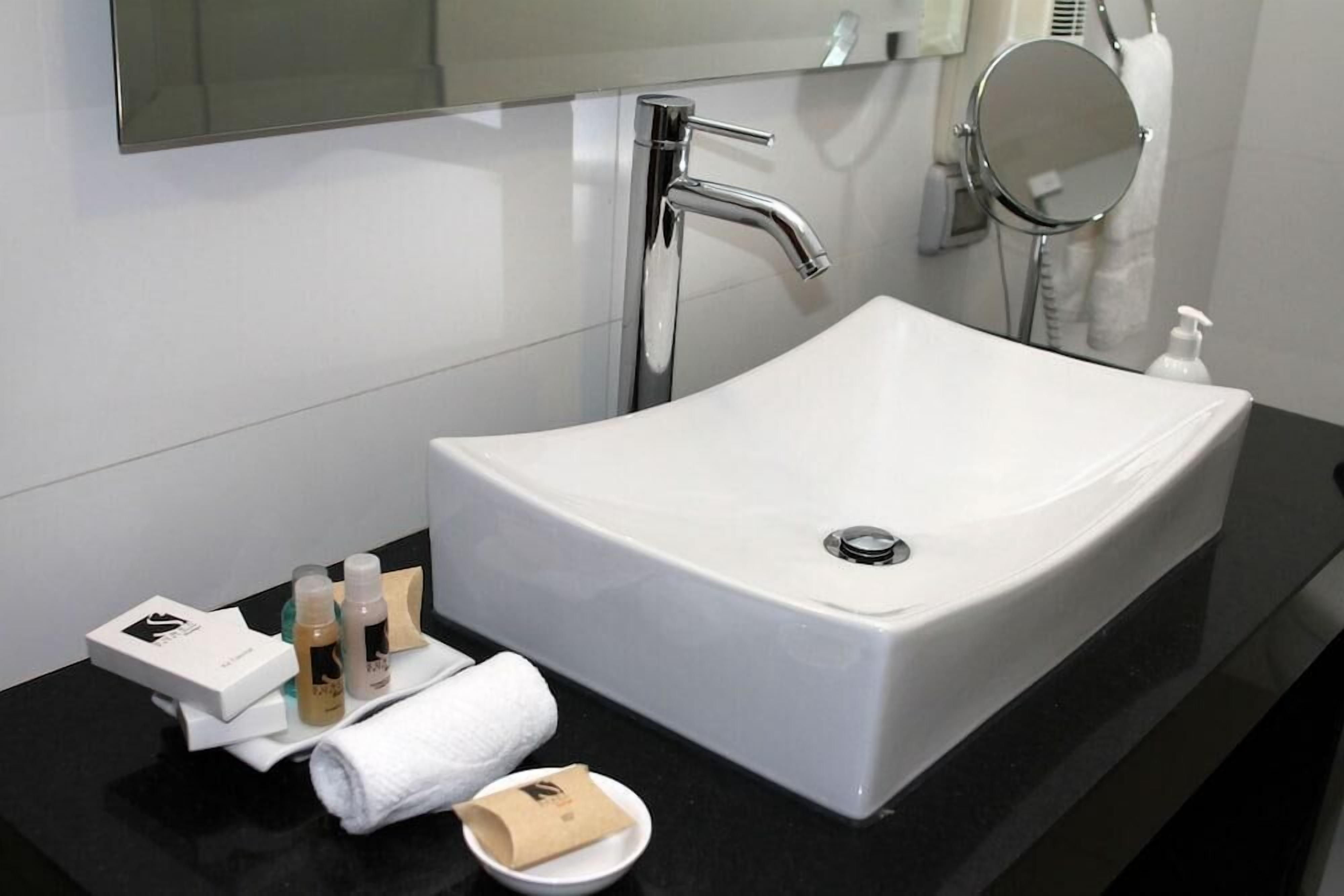 A modern bathroom with a white sink, chrome faucet, and a large mirror.