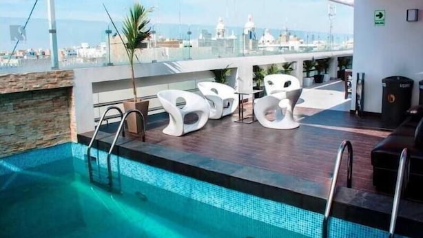 A rooftop pool area with a clear view of the city skyline, a stone wall, and modern white lounge chairs. - Sunec Hotel (Chiclayo)