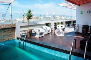 A rooftop pool area with a clear view of the city skyline, a stone wall, and modern white lounge chairs. - Sunec Hotel (Chiclayo)