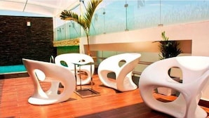 A reception area with modern white chairs, a stone wall, and a view of a building through a glass wall. - Sunec Hotel (Chiclayo)