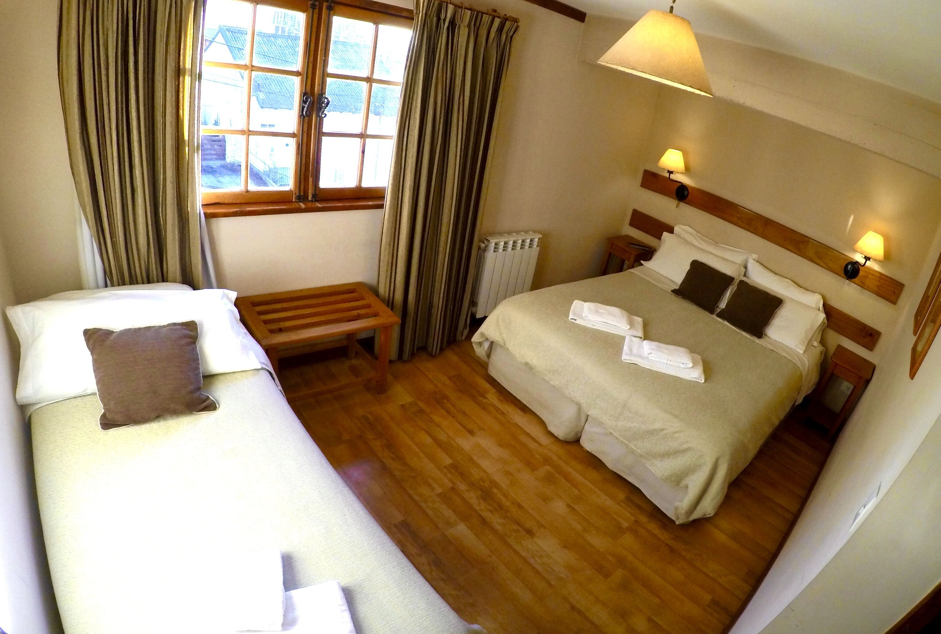 Habitación de hotel con dos camas, un banco de madera, un radiador y una ventana con cortinas.