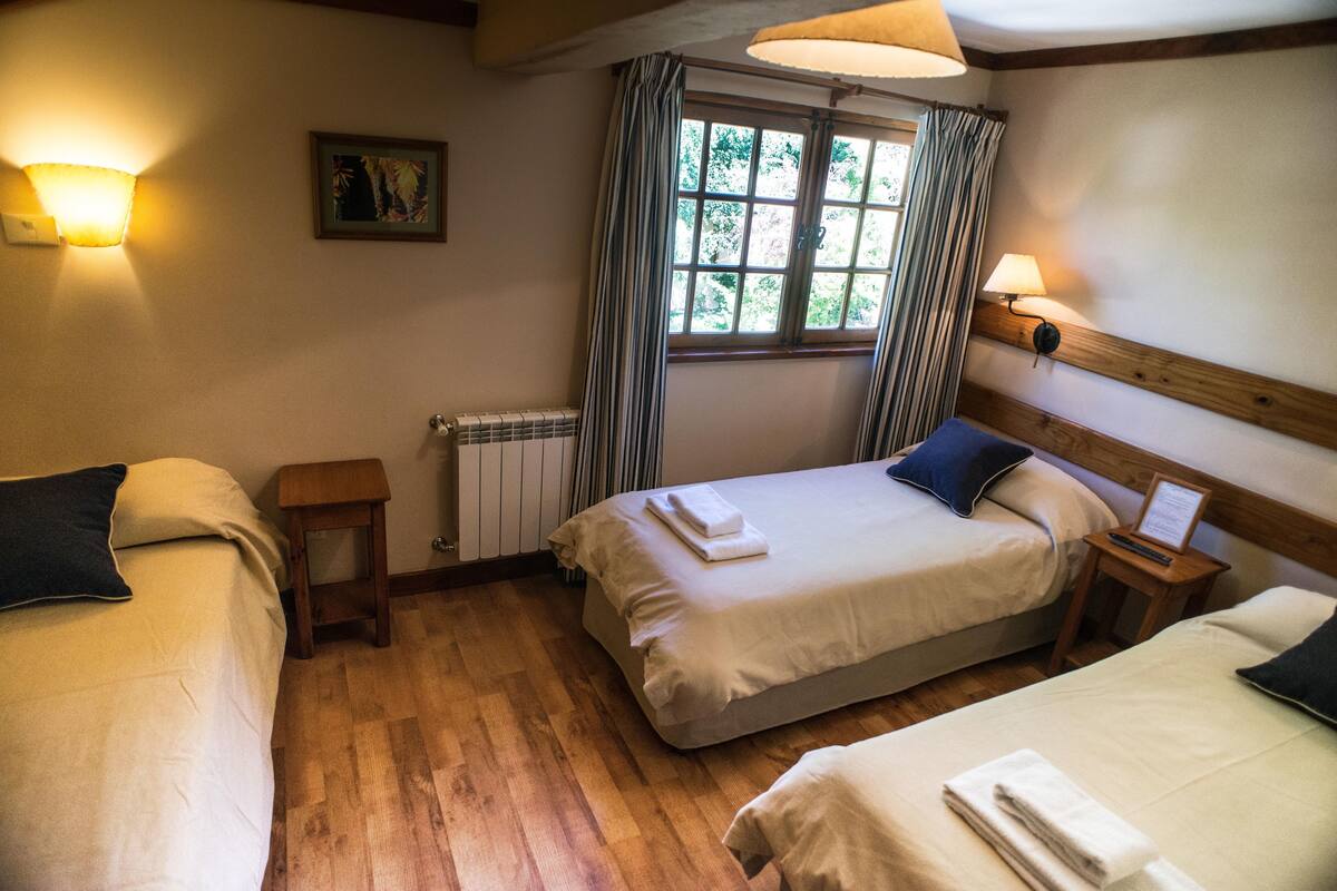 Una habitación de hotel con dos camas, una ventana con cortinas, un radiador y lámparas fijadas a la pared.