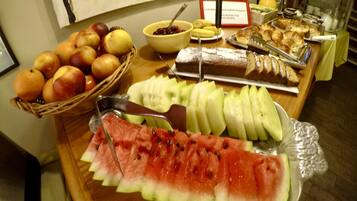 A buffet with sliced watermelon, apples, oranges, and various pastries.