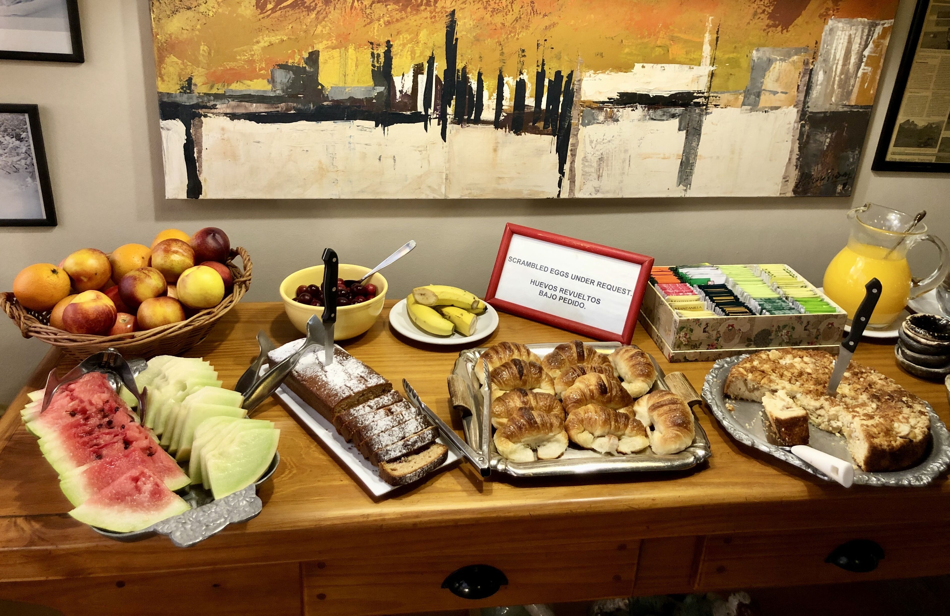 A breakfast buffet with fruits, pastries, and a sign indicating scrambled eggs are under request.
