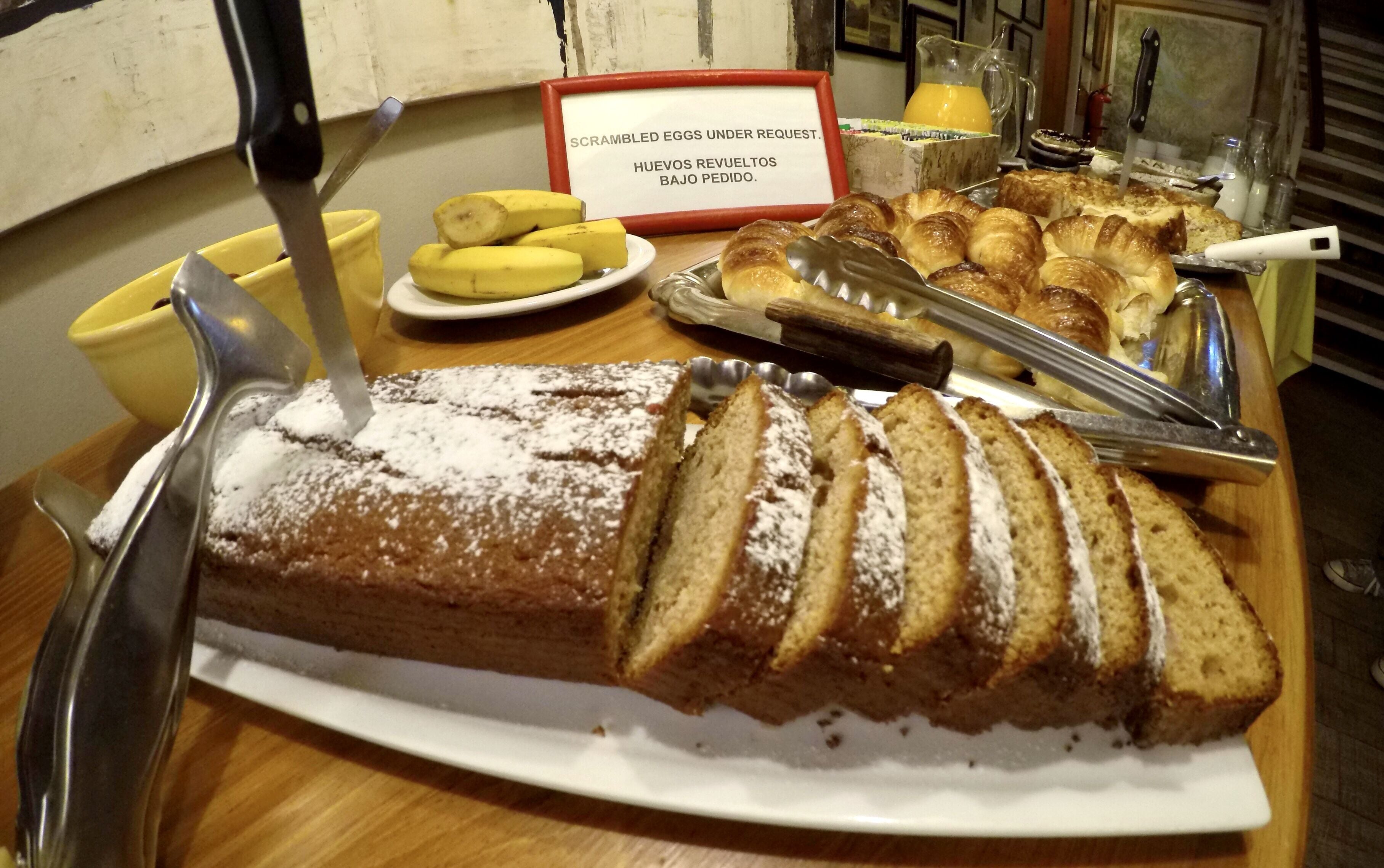 A breakfast buffet with a variety of pastries, including a cake with powdered sugar, bananas, and croissants.