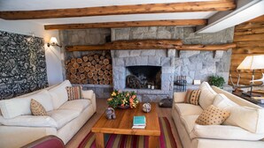 Una sala de estar acogedora con chimenea de piedra, dos sofás, una mesa de centro con libros y un colorido tapete a rayas.